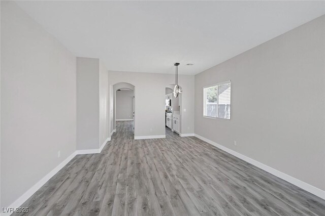 unfurnished dining area with arched walkways, light wood-type flooring, and baseboards