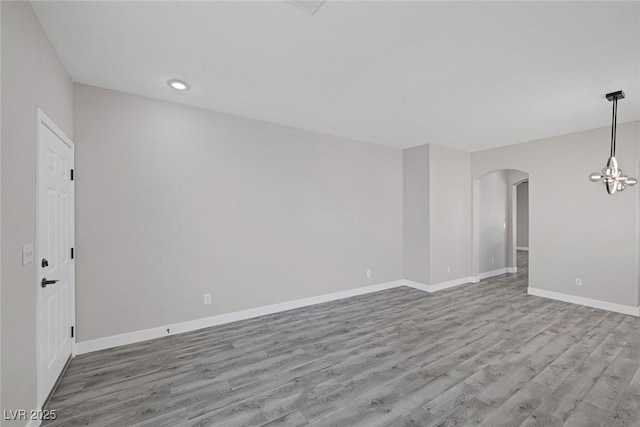 empty room featuring arched walkways, wood finished floors, baseboards, recessed lighting, and a chandelier