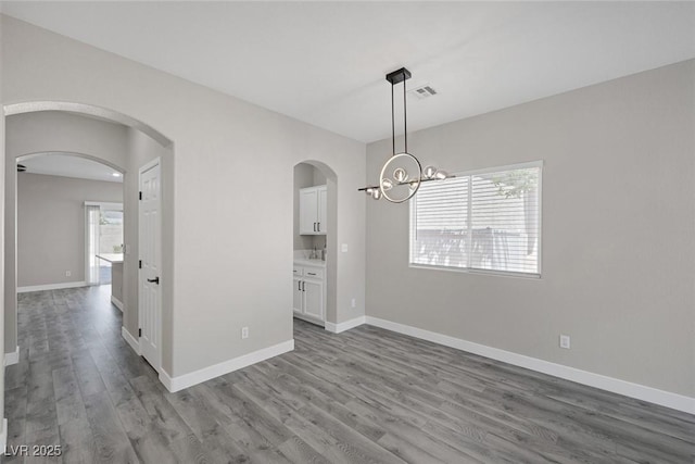 unfurnished room with wood finished floors, arched walkways, baseboards, and a chandelier