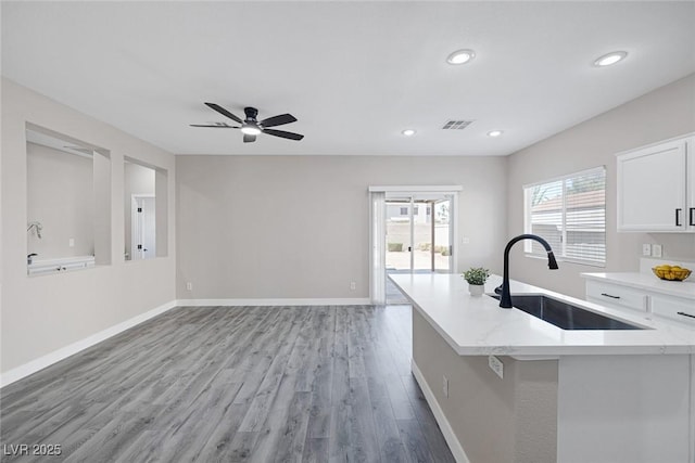 kitchen featuring a sink, white cabinetry, light wood-style flooring, ceiling fan, and baseboards