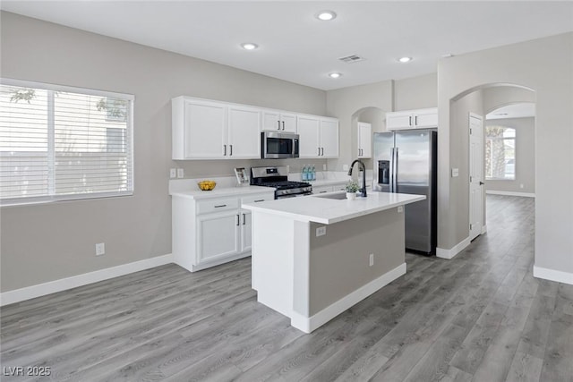 kitchen with appliances with stainless steel finishes, a sink, arched walkways, white cabinets, and recessed lighting