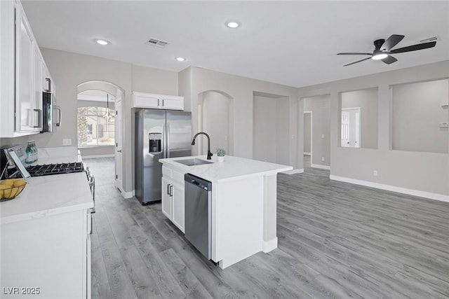 kitchen with stainless steel appliances, a sink, arched walkways, ceiling fan, and light wood finished floors