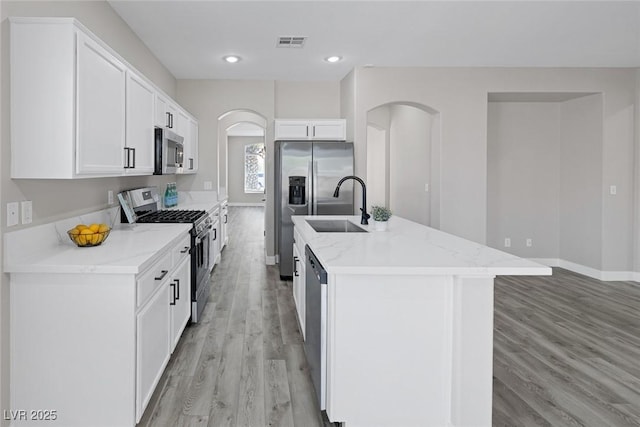 kitchen with appliances with stainless steel finishes, light wood-style floors, a sink, a kitchen island with sink, and white cabinetry