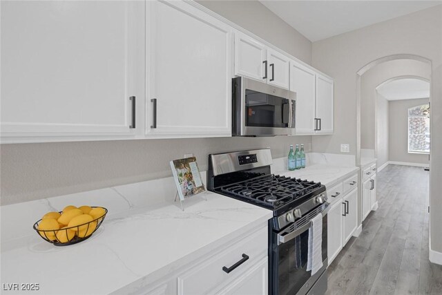 kitchen with appliances with stainless steel finishes, arched walkways, white cabinetry, and light stone counters