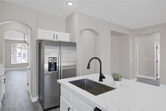 kitchen with stainless steel fridge, a sink, light stone countertops, white cabinetry, and arched walkways