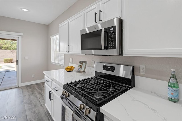 kitchen featuring appliances with stainless steel finishes, white cabinets, light stone counters, light wood-type flooring, and recessed lighting