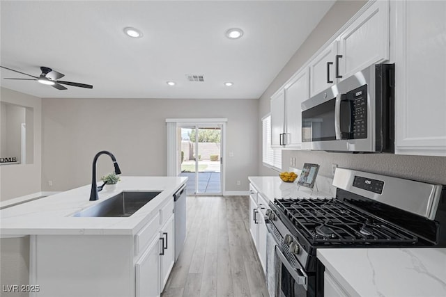 kitchen with appliances with stainless steel finishes, a sink, light wood finished floors, white cabinetry, and light stone counters
