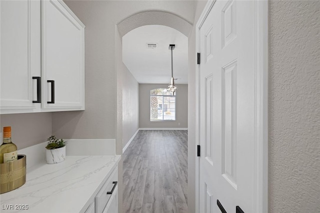 hall featuring light wood-style floors, a chandelier, arched walkways, a textured wall, and baseboards
