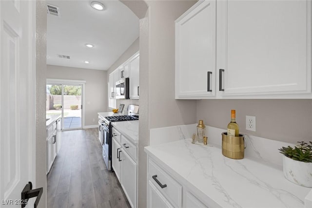 kitchen with stainless steel appliances, white cabinets, light stone countertops, wood finished floors, and recessed lighting
