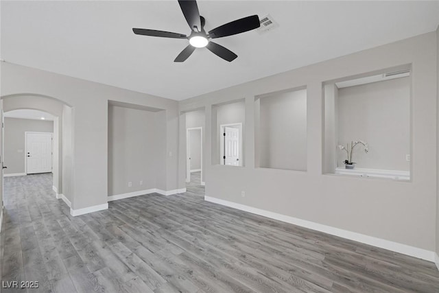 unfurnished living room with ceiling fan, wood finished floors, baseboards, and arched walkways