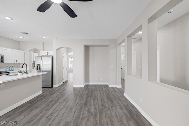 unfurnished living room featuring a ceiling fan, arched walkways, wood finished floors, recessed lighting, and baseboards
