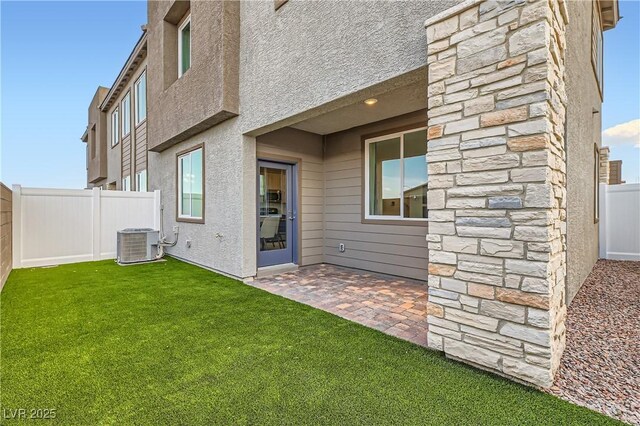 back of property with central air condition unit, stone siding, and a patio