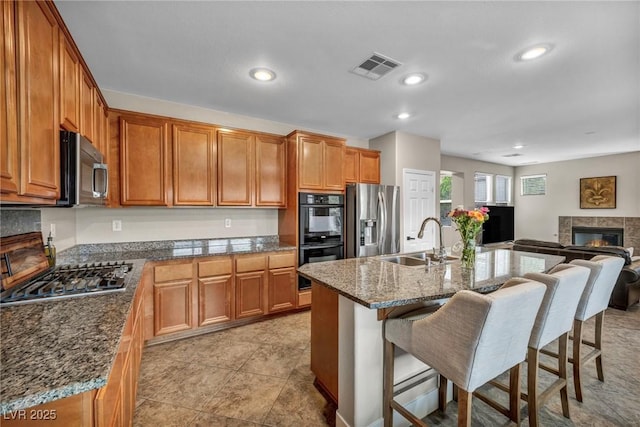kitchen with a sink, appliances with stainless steel finishes, a breakfast bar, a tiled fireplace, and brown cabinets