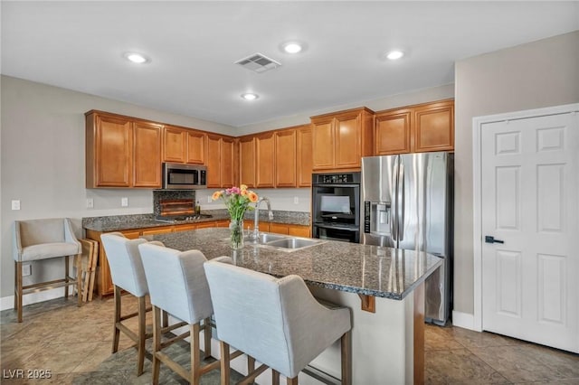 kitchen featuring appliances with stainless steel finishes, a sink, baseboards, an island with sink, and a breakfast bar area