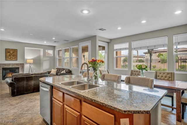 kitchen featuring a sink, dishwasher, open floor plan, a center island with sink, and a tile fireplace