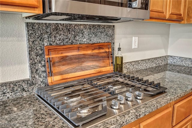kitchen view of brown cabinets, stainless steel appliances, and dark stone counters