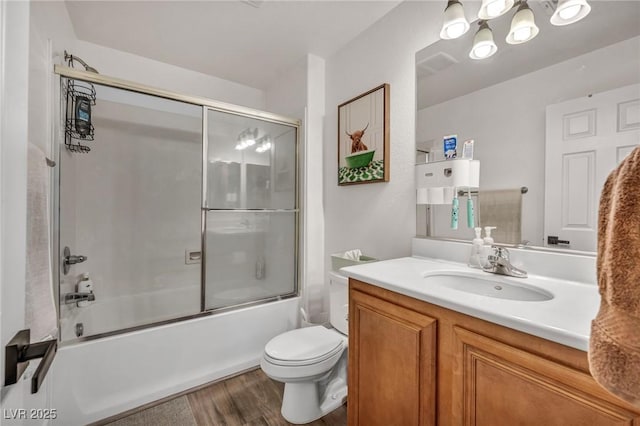 full bath with wood finished floors, bath / shower combo with glass door, vanity, toilet, and a chandelier