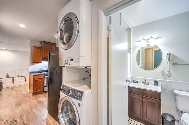 1553 Dorothy Ave Unit 4, Las Vegas, NV 89119 - laundry room with stacked washer / dryer, a wainscoted wall, light wood-type flooring, and tile walls