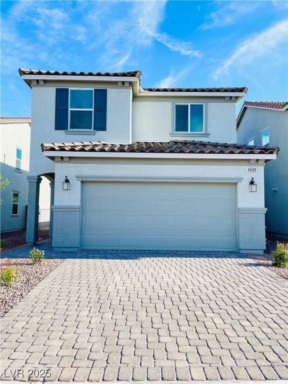 mediterranean / spanish house with a tiled roof, a garage, and decorative driveway