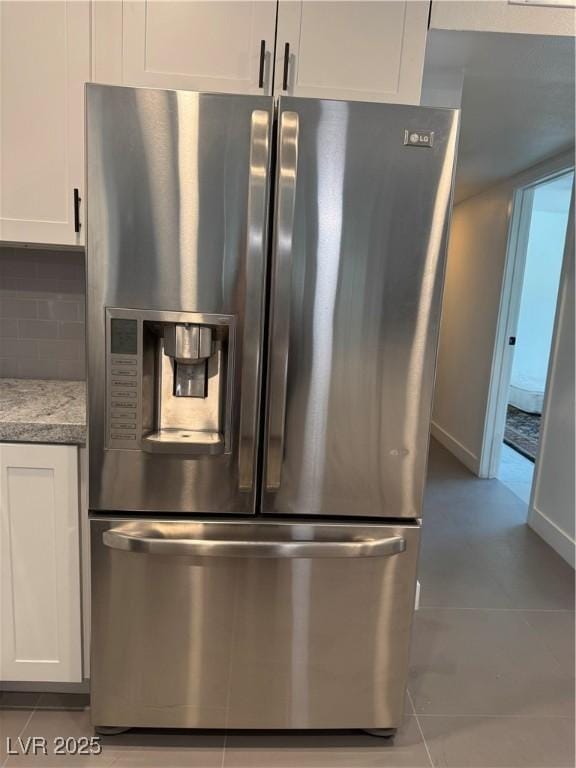 detailed view of stainless steel refrigerator with ice dispenser, white cabinets, decorative backsplash, and light stone counters