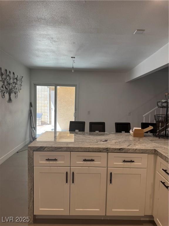 kitchen with white cabinets, light stone countertops, a textured ceiling, baseboards, and a peninsula