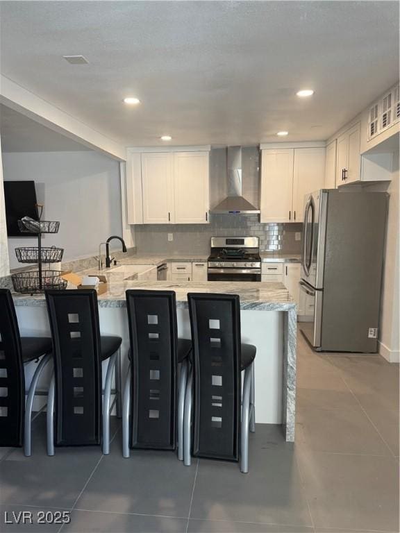 kitchen featuring wall chimney exhaust hood, stainless steel appliances, a peninsula, white cabinetry, and a sink