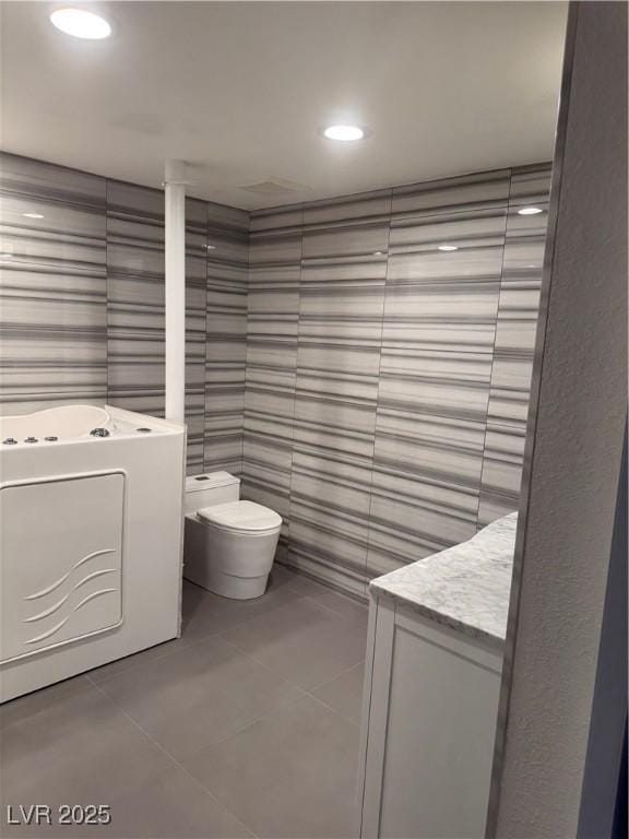 full bathroom featuring tile patterned flooring, toilet, vanity, a tub, and tile walls