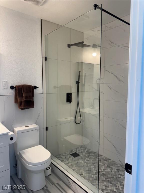 bathroom featuring a stall shower, toilet, tile walls, vanity, and marble finish flooring