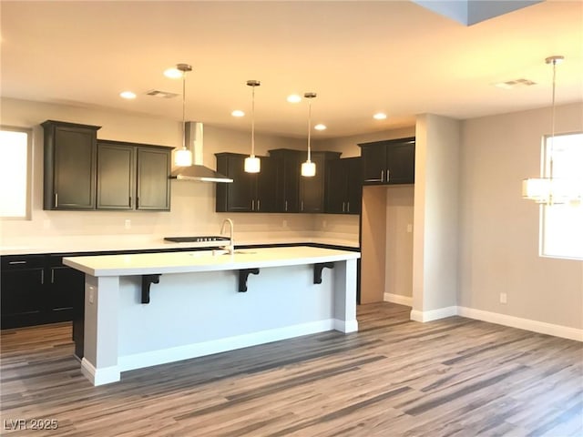 1027 Cambridge Park St, Las Vegas, NV 89148 - kitchen with wall chimney exhaust hood, wood finished floors, light countertops, a kitchen island with sink, and recessed lighting