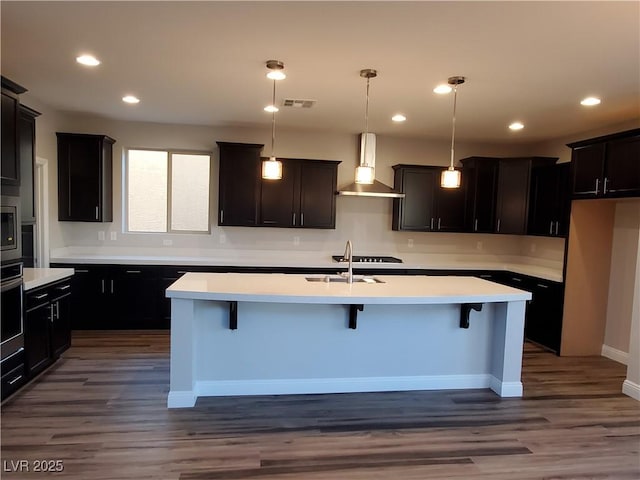 1027 Cambridge Park St, Las Vegas, NV 89148 - kitchen featuring wall chimney exhaust hood, a sink, light countertops, a kitchen island with sink, and dark wood-style floors