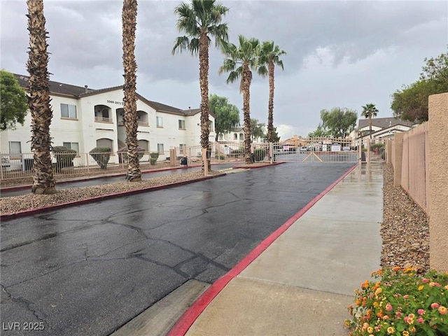 view of asphalt road with a residential view, a gate, curbs, and a gated entry