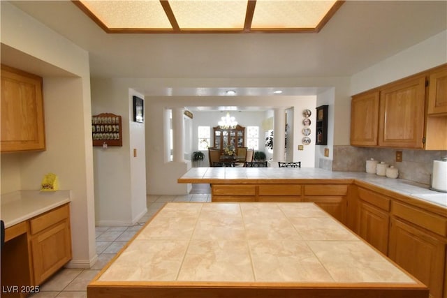 kitchen with tile counters, a chandelier, a peninsula, light tile patterned flooring, and tasteful backsplash