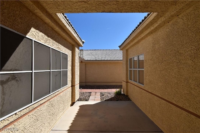 view of side of property with stucco siding, a patio area, a tile roof, and fence
