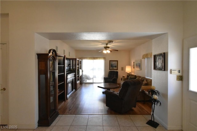 living area featuring light tile patterned floors, a ceiling fan, and baseboards