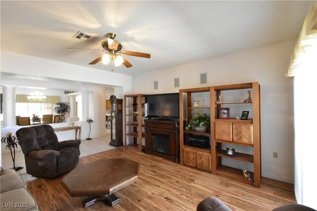 living area with a chandelier, ceiling fan, light wood-style floors, a fireplace, and decorative columns