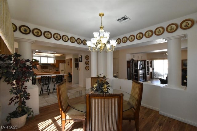 dining area featuring ornate columns, a chandelier, and wood finished floors