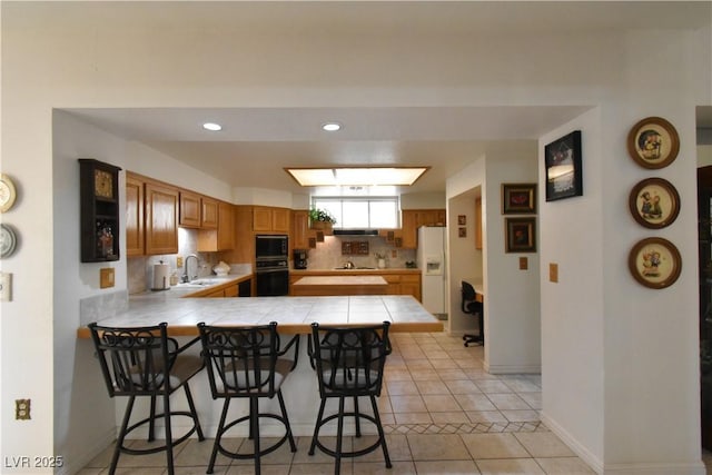 kitchen featuring black appliances, a sink, tile counters, a peninsula, and a breakfast bar