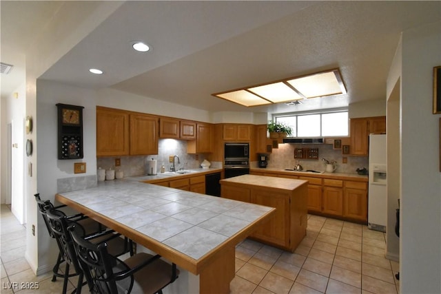 kitchen with black appliances, a sink, backsplash, light tile patterned flooring, and tile counters