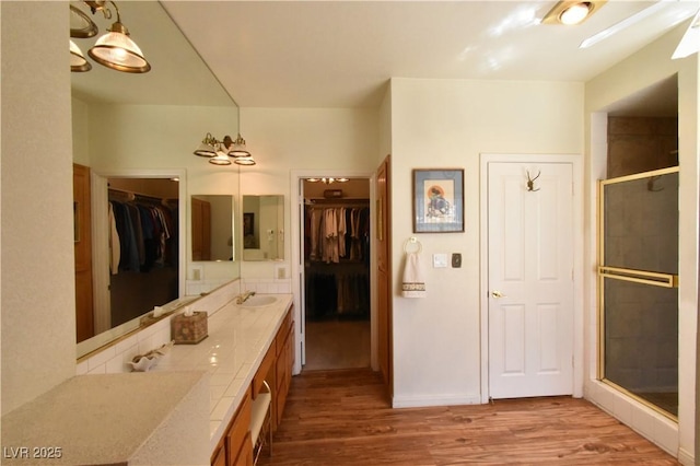 bathroom with wood finished floors, a stall shower, double vanity, and a walk in closet