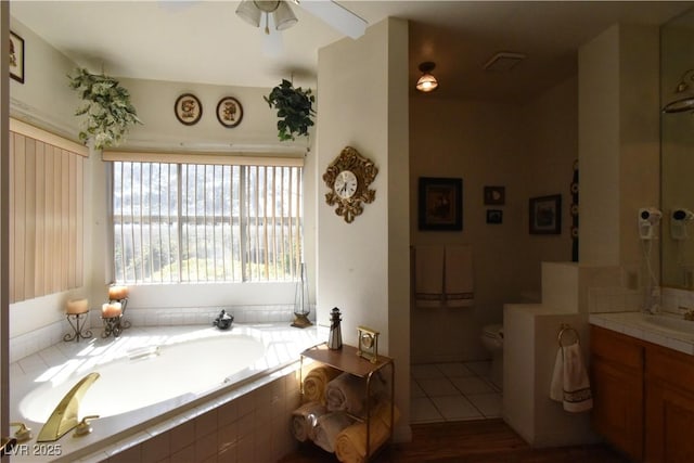 bathroom featuring toilet, a bath, vanity, wood finished floors, and a ceiling fan