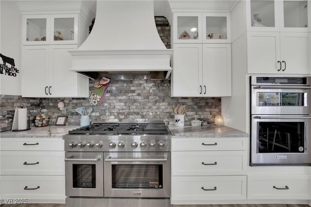 7211 Heggie Ave, Las Vegas, NV 89131 - kitchen featuring stainless steel appliances, premium range hood, tasteful backsplash, and white cabinetry