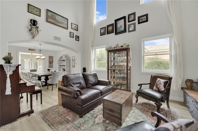 7211 Heggie Ave, Las Vegas, NV 89131 - living room with arched walkways, a high ceiling, a chandelier, and light wood-style floors