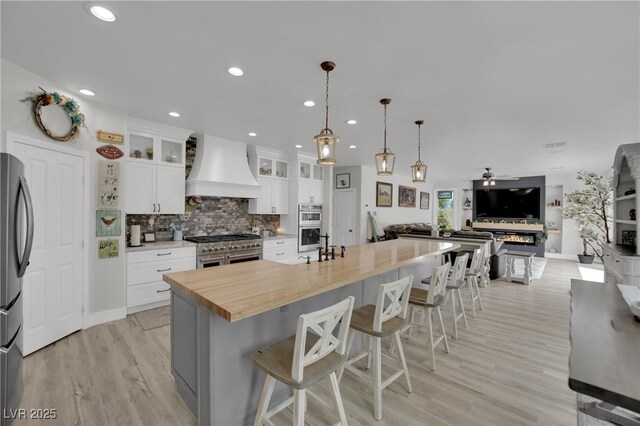 7211 Heggie Ave, Las Vegas, NV 89131 - kitchen with custom exhaust hood, stainless steel appliances, open floor plan, backsplash, and white cabinets