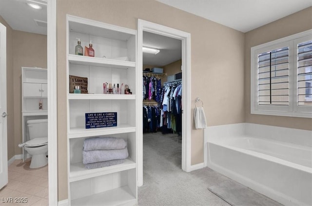 bathroom featuring a garden tub, toilet, a walk in closet, and baseboards