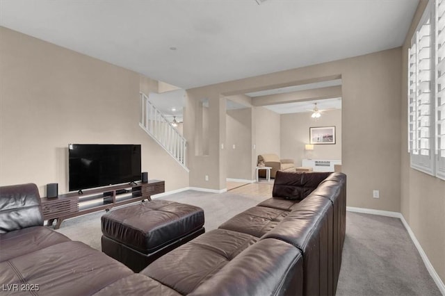 living area featuring carpet, stairs, baseboards, and ceiling fan