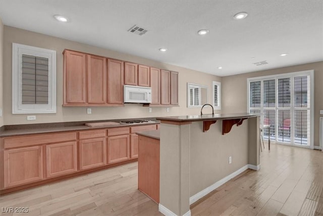 kitchen featuring white appliances, light wood-type flooring, an island with sink, recessed lighting, and baseboards