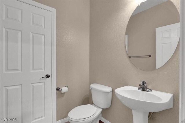 half bath with baseboards, toilet, and a sink