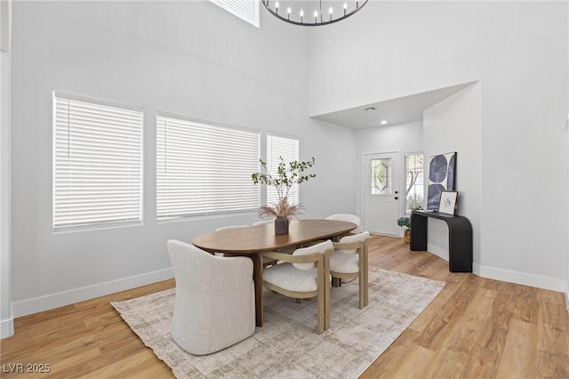dining area featuring baseboards, light wood-type flooring, a chandelier, and a high ceiling