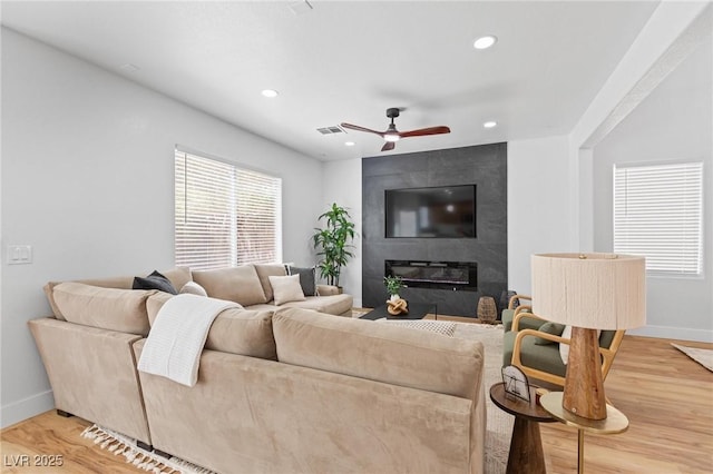 living room featuring baseboards, light wood-type flooring, recessed lighting, a large fireplace, and a ceiling fan