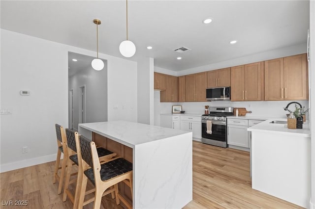 kitchen featuring stainless steel appliances, a sink, light wood finished floors, a kitchen island, and hanging light fixtures